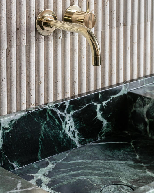 Florence marble vanity detail in green natural stone with integrated sink and brass wall-mounted faucet