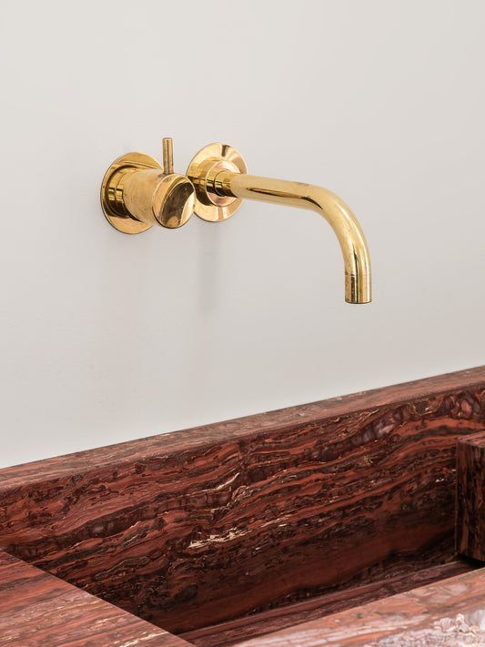 Close up of Genoa marble vanity showing red natural stone veining and wall mounted brass faucet detail