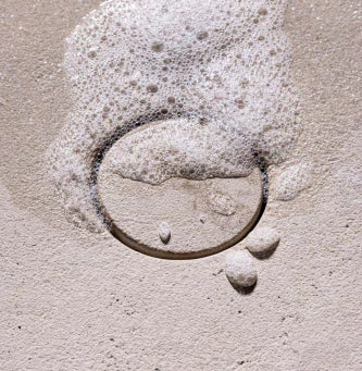 detail of anfora round natural stone bathtub drain with water and soap bubbles