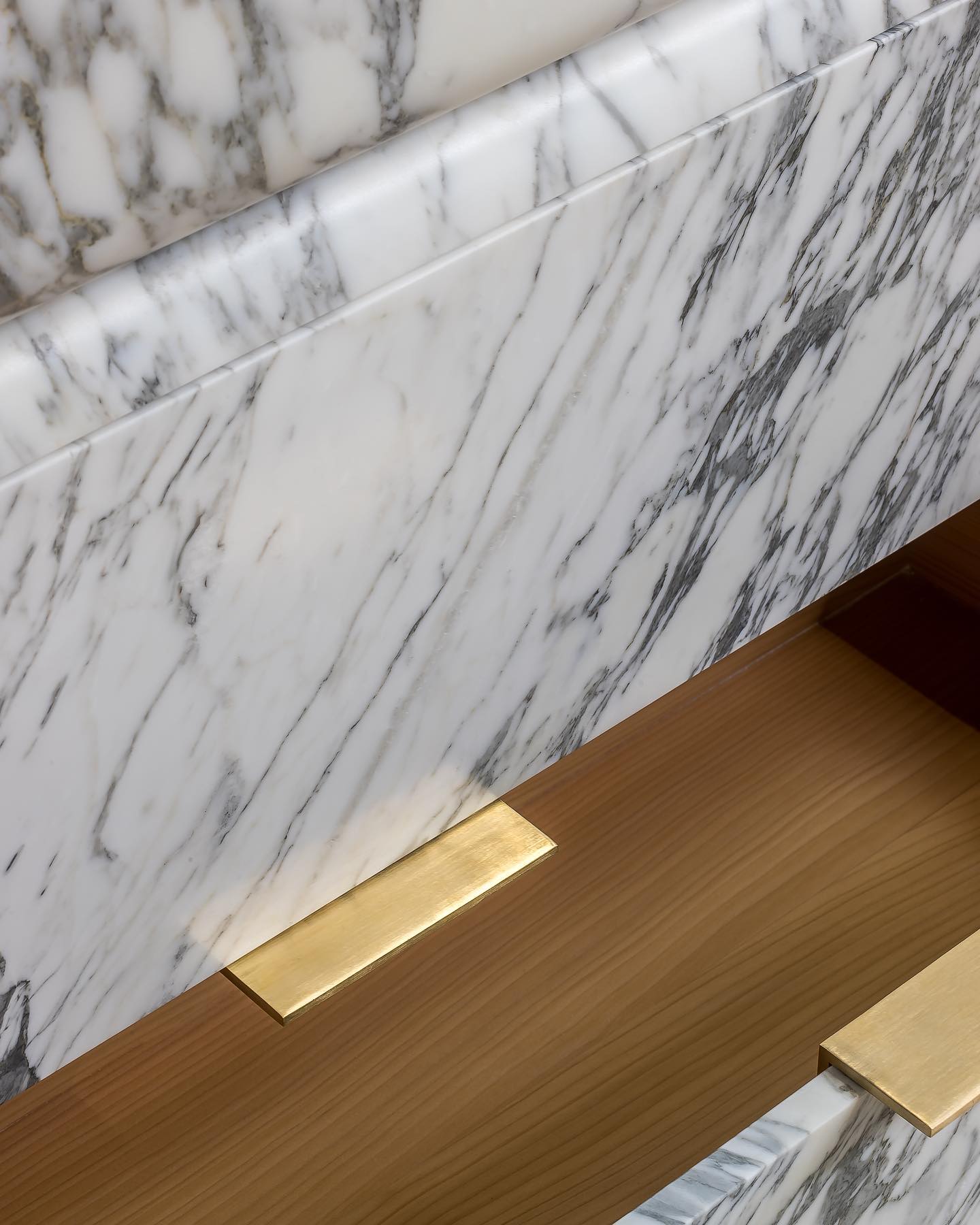 Close-up of marble vanity with natural veining and brushed brass handle detail