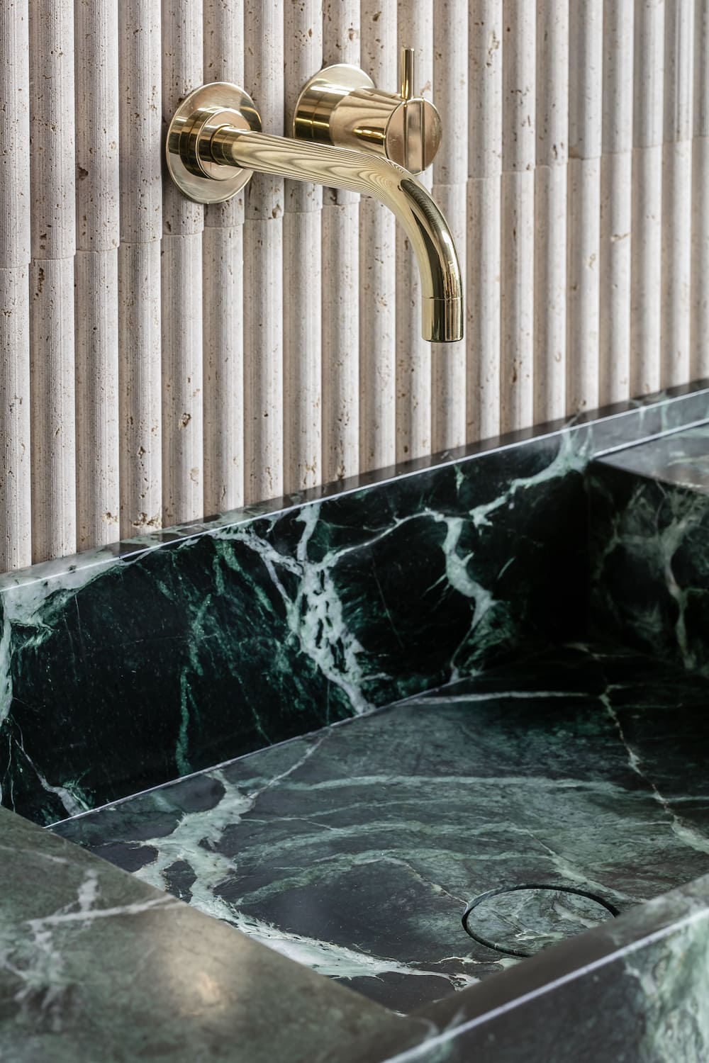 Florence marble vanity with green stone basin and wall mounted brass faucet detail in luxury bathroom