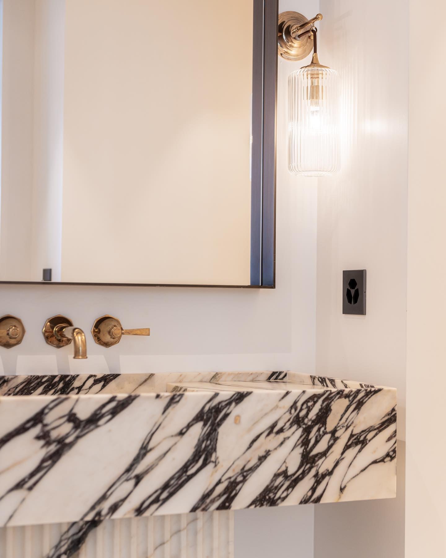 Florence marble vanity with mirror and wall light detail in luxury bathroom interior with brass fixtures