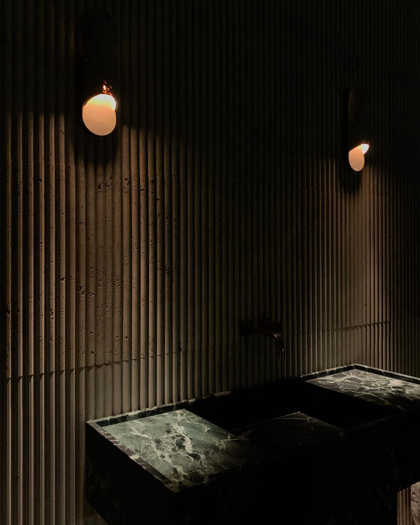 Florence marble vanity in green stone shown in moody low lighting bathroom with textured wall and ambient lighting