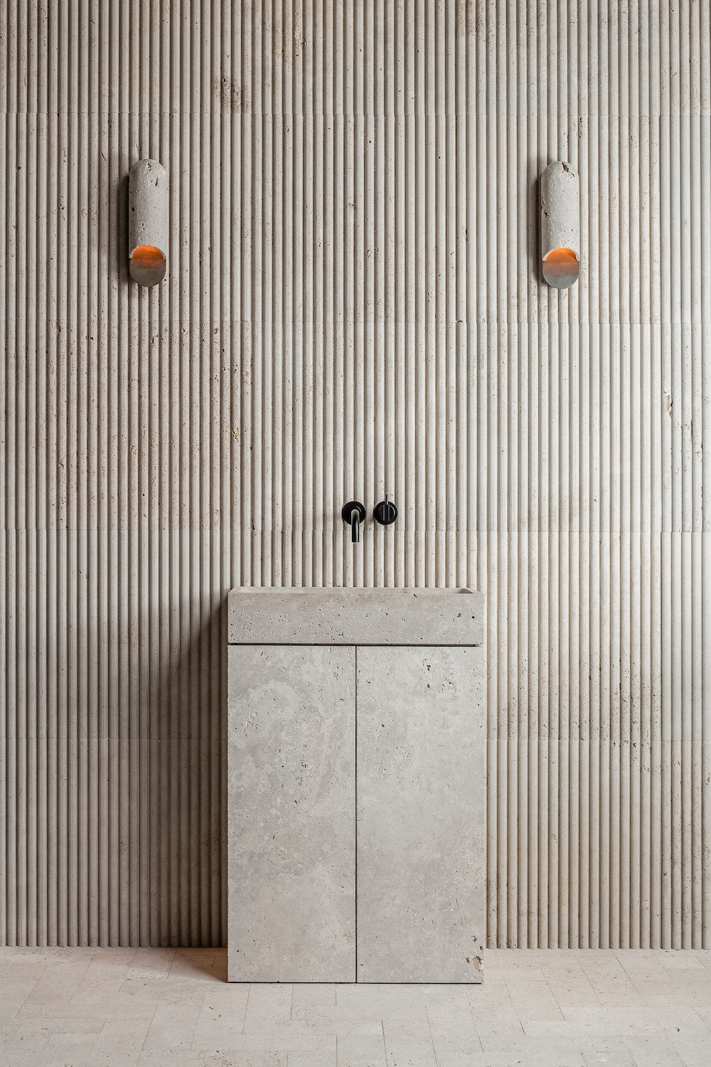 Minimalist stone bathroom vanity integrated in architectural interior with fluted wall and wall lighting