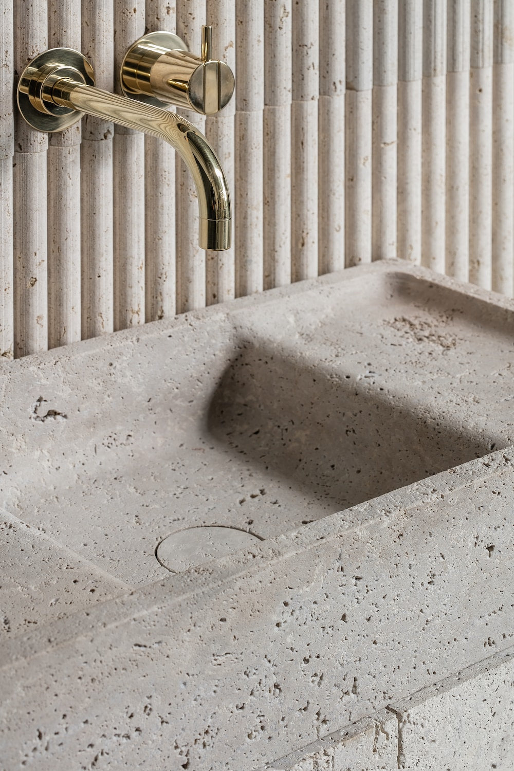 Stone bathroom vanity sink detail with brass wall-mounted faucet and textured surface