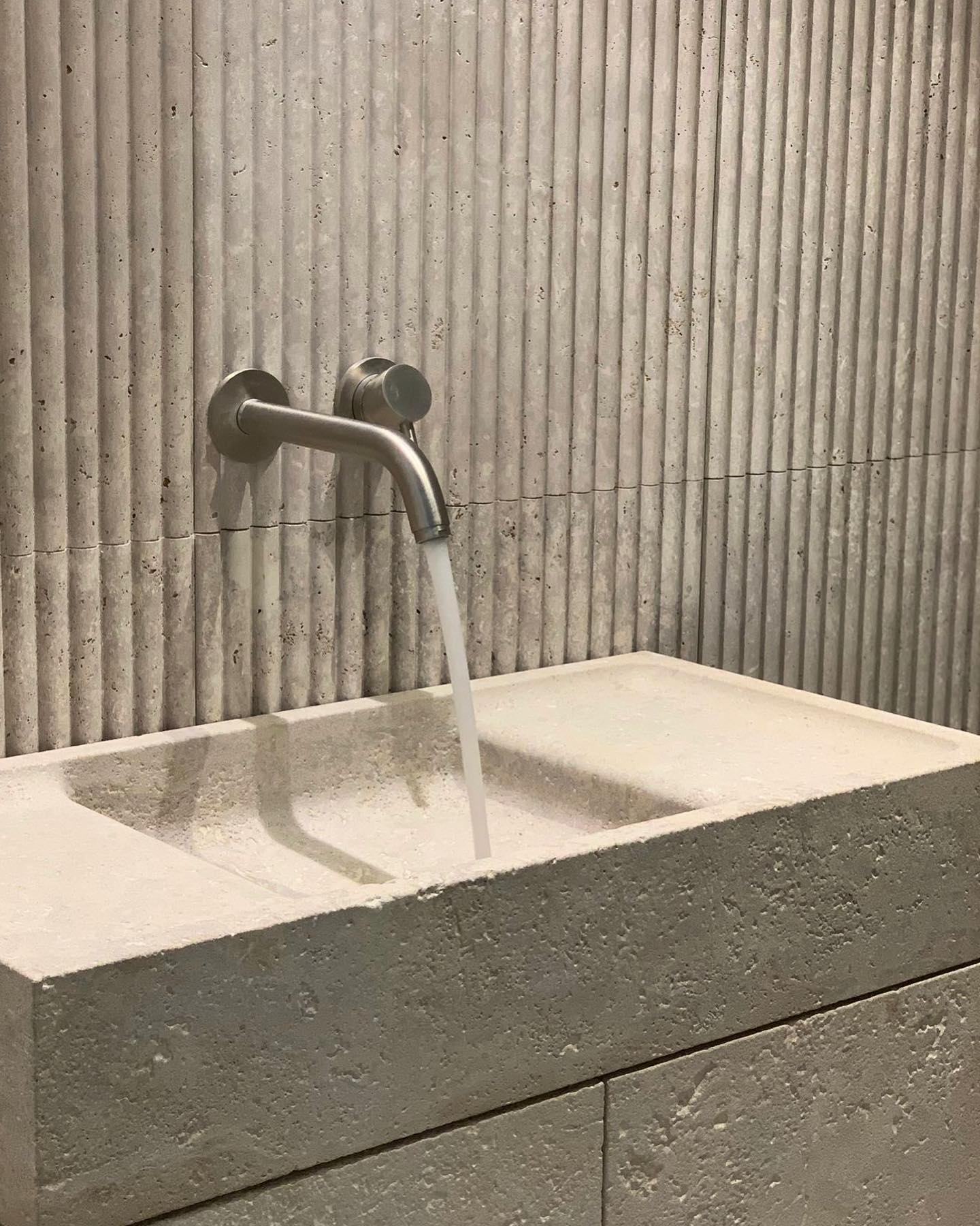 Stone bathroom vanity with integrated sink and running water from wall-mounted faucet