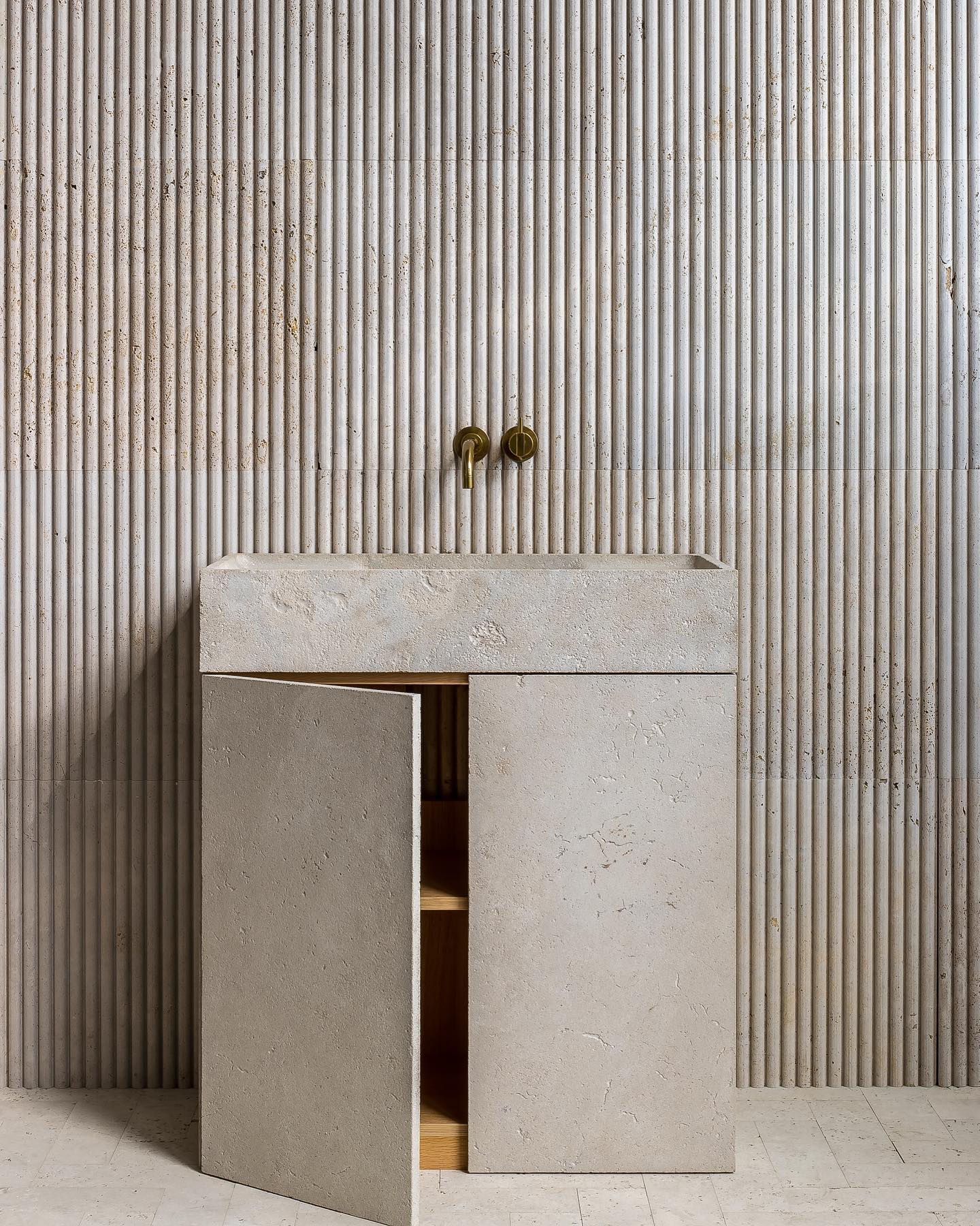 Stone bathroom vanity with open cabinet showing interior storage and natural texture finish