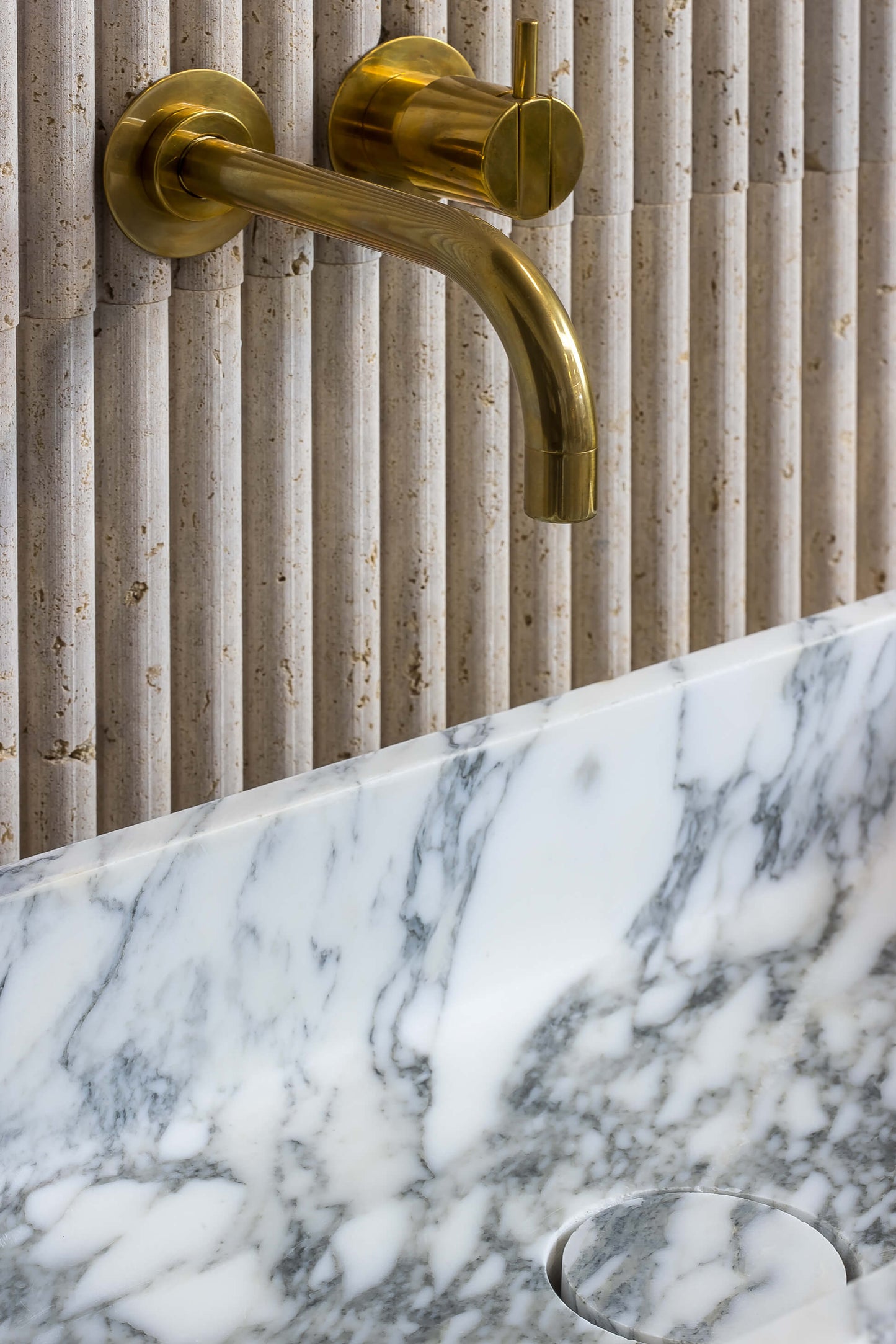 Close up of Milan marble sink in Arabescato stone with brass wall faucet and natural stone veining Eden Stone Designs