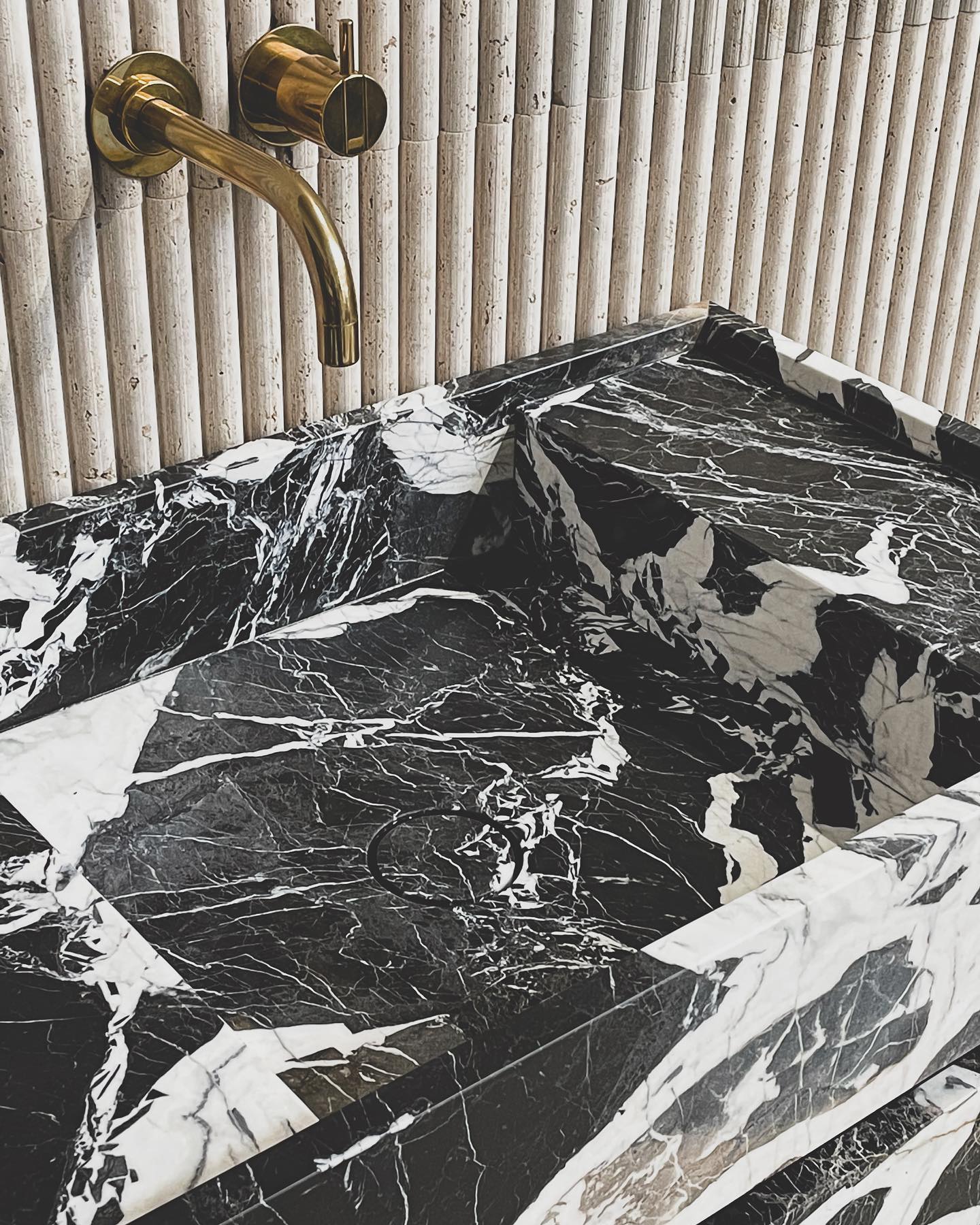 Close-up of Venice black marble vanity basin with bold white veining and brass wall-mounted faucet in luxury bathroom