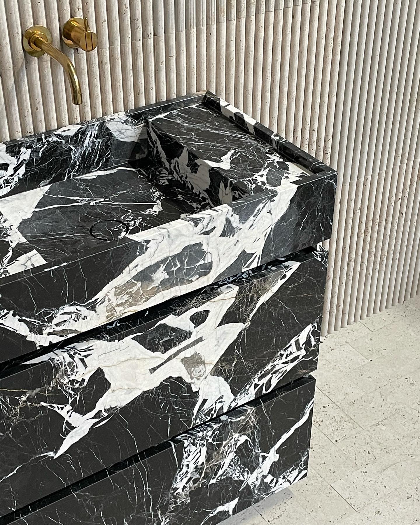 Venice black marble vanity with bold white veining in a luxury bathroom with fluted stone wall and brass faucet