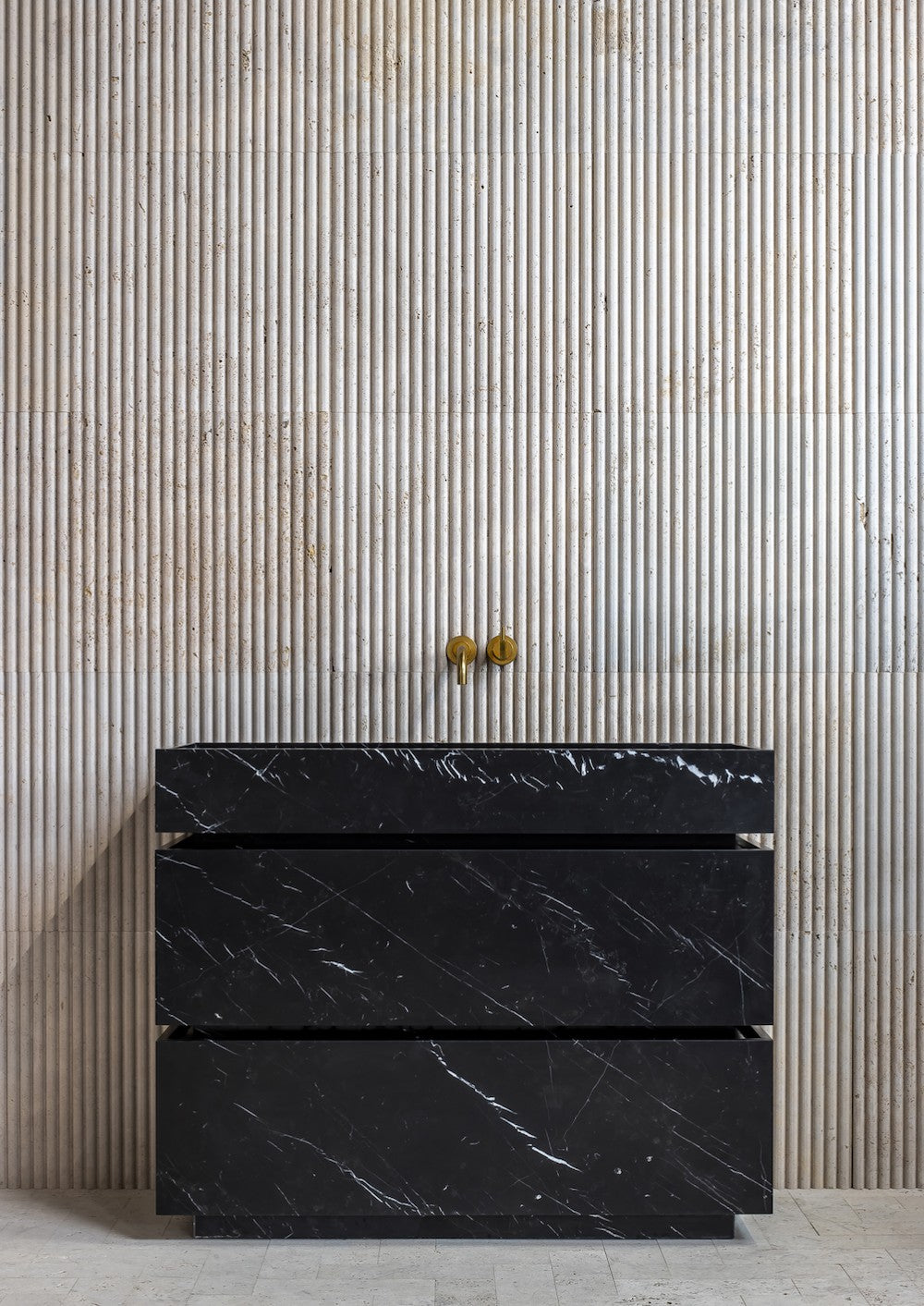 Venice black marble vanity front view in a minimalist bathroom with fluted stone wall and brass faucet