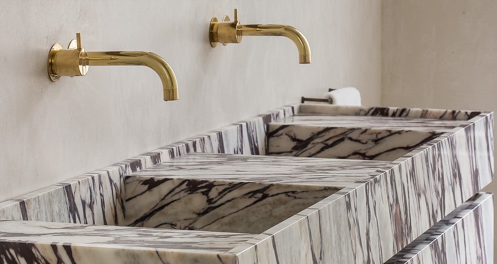 Close-up of Venice double marble vanity with integrated basins and brass wall-mounted faucets in luxury bathroom