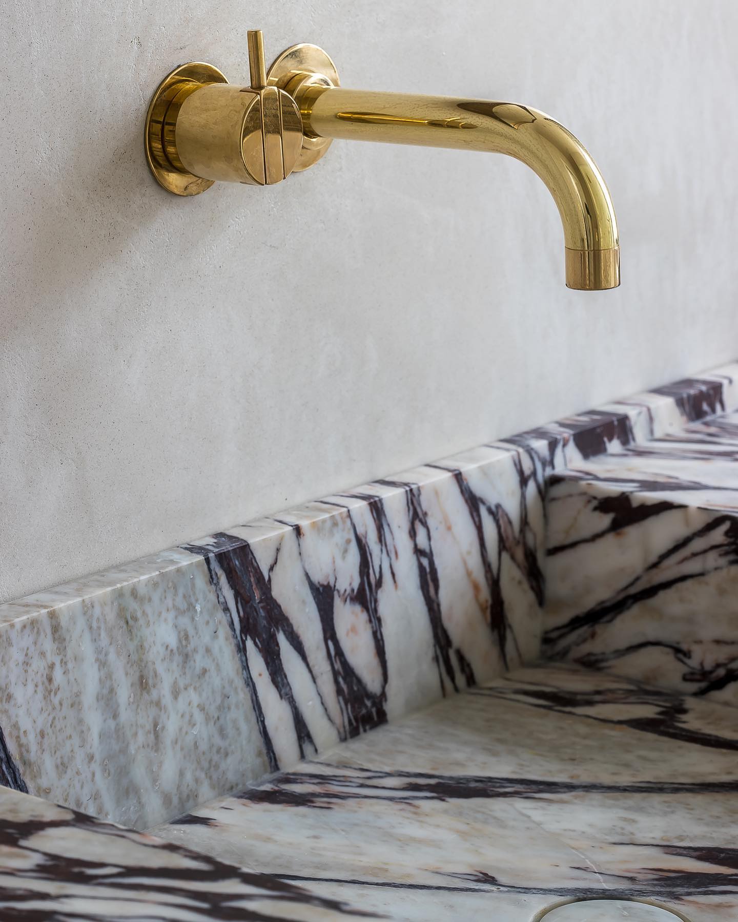 Detail of Calacatta marble vanity with integrated basin and polished brass wall-mounted faucet