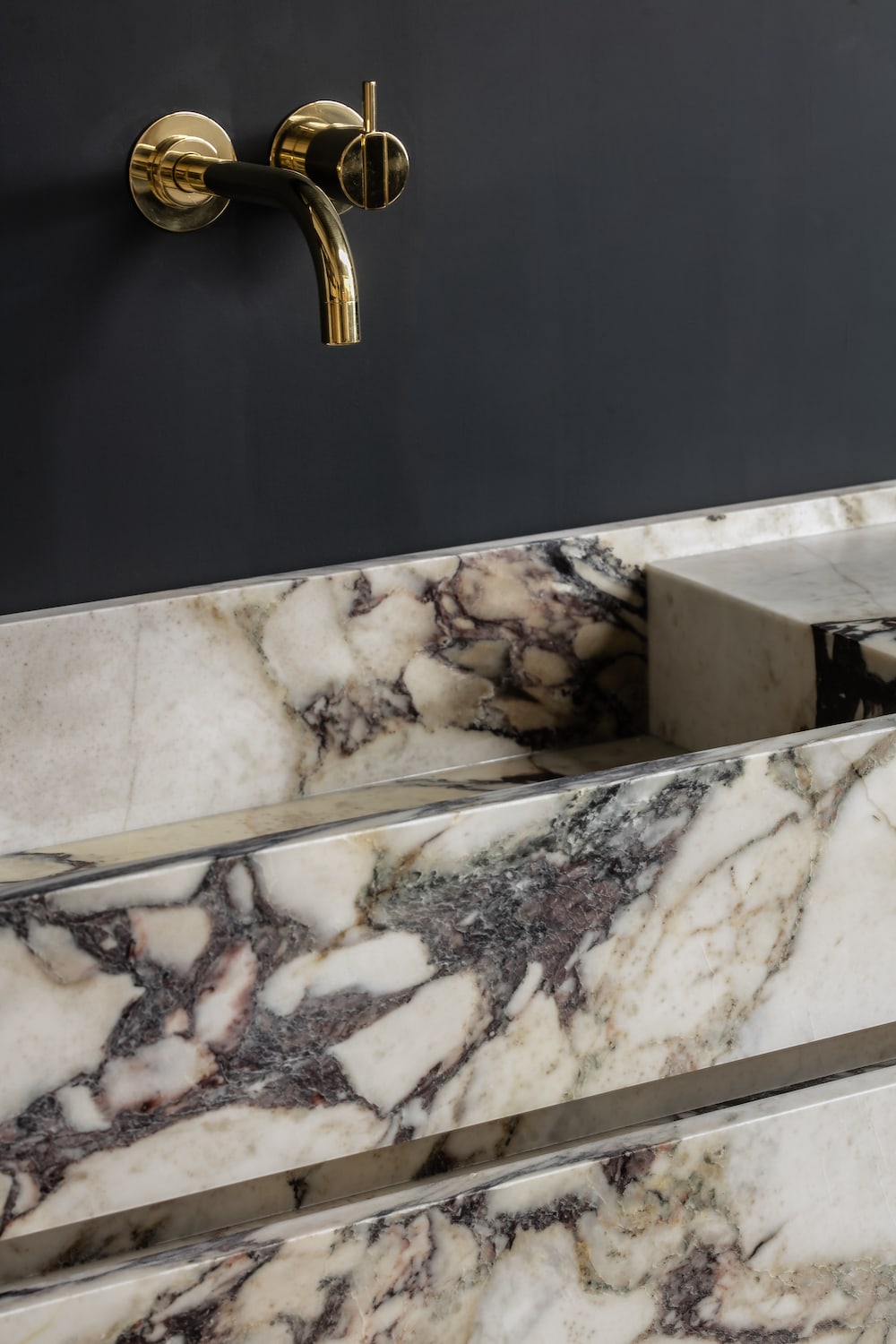 Close up of Venice marble vanity backsplash with Calacatta Viola veining and wall mounted brass faucet