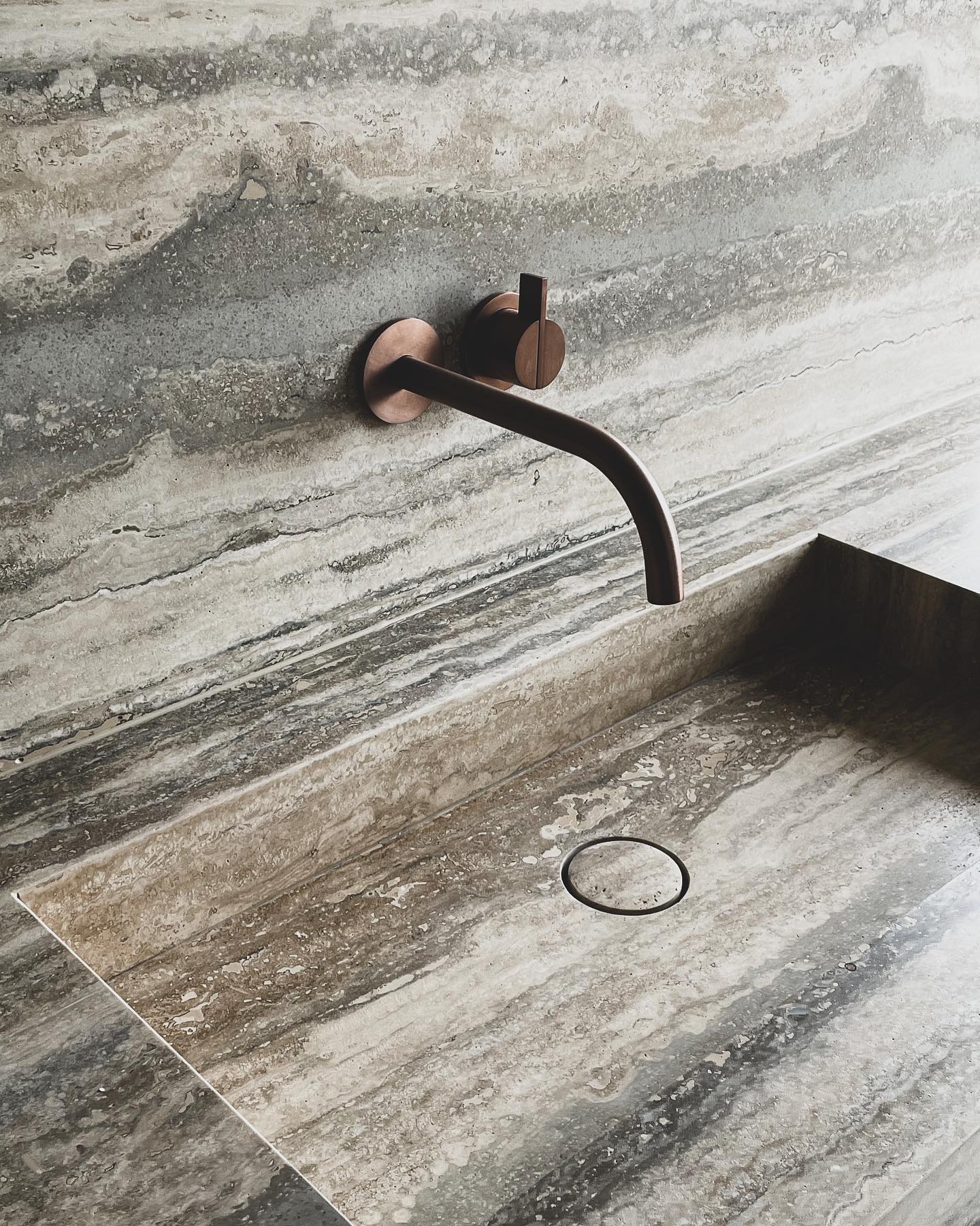 Venice travertine vanity basin with natural stone texture and bronze wall-mounted faucet in minimalist bathroom