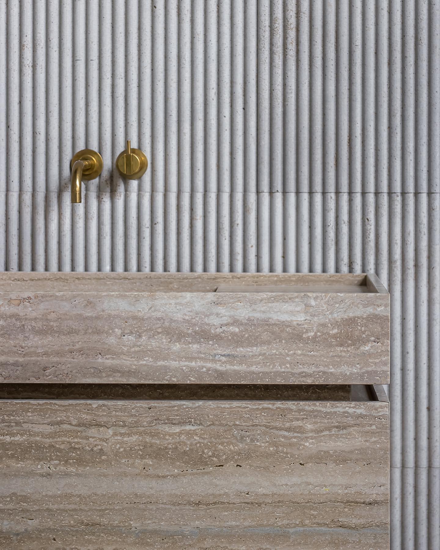 Close-up of Venice travertine vanity with natural stone texture, fluted wall background and brass wall-mounted faucet