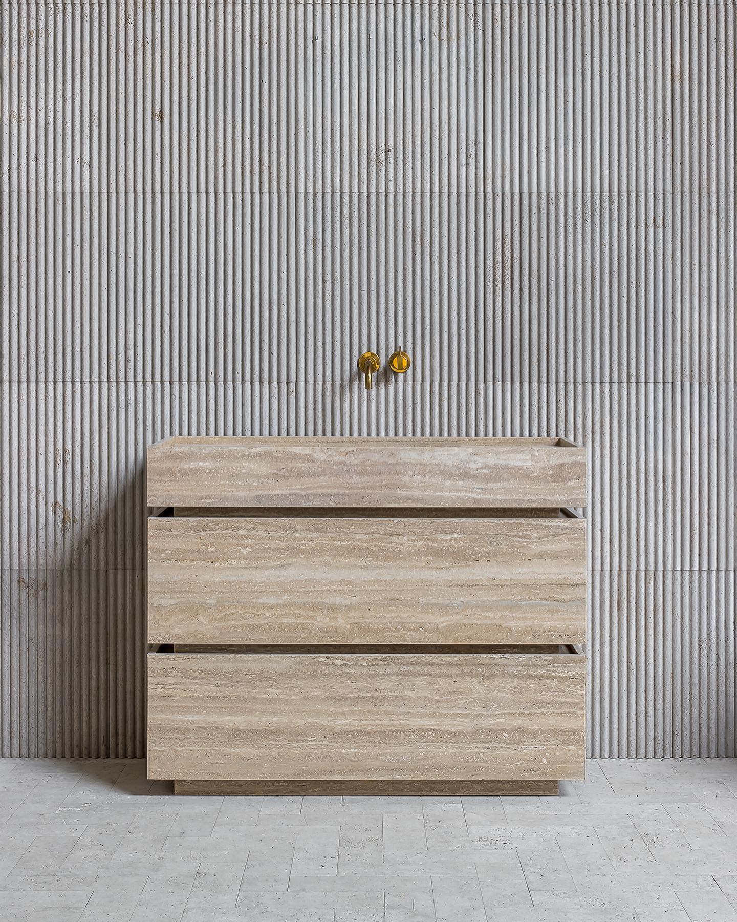 Venice travertine marble vanity in a minimalist bathroom with fluted stone wall and brass faucet